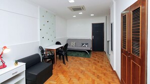 A compact room with a sofa, a small table, a desk, and a chair. There is a door with a window and a wooden door frame. - Rio Spot C058 (Rio de Janeiro)
