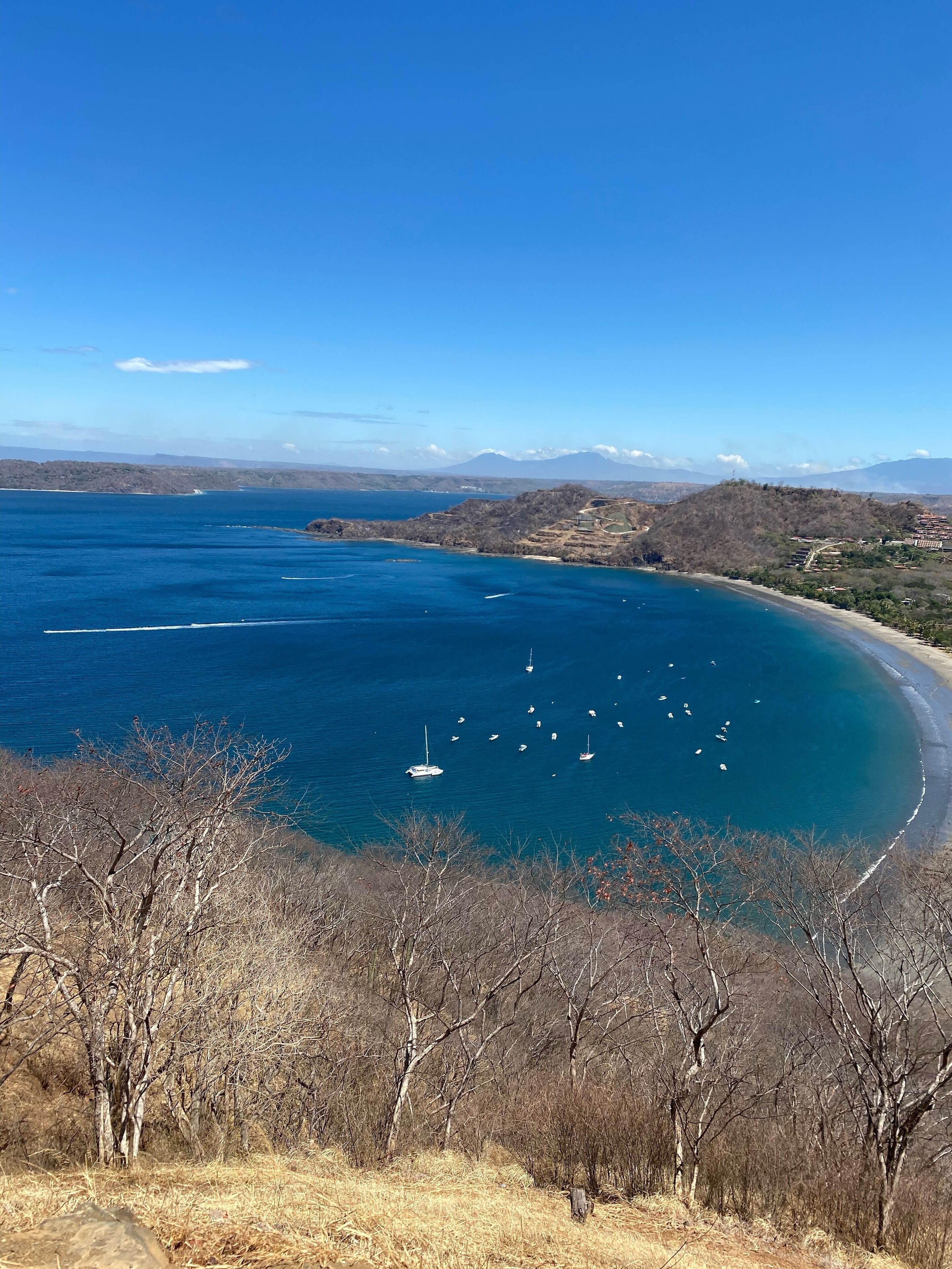 Un paysage côtier offrant une vue dégagée sur la mer, des bateaux et un terrain vallonné en arrière-plan.