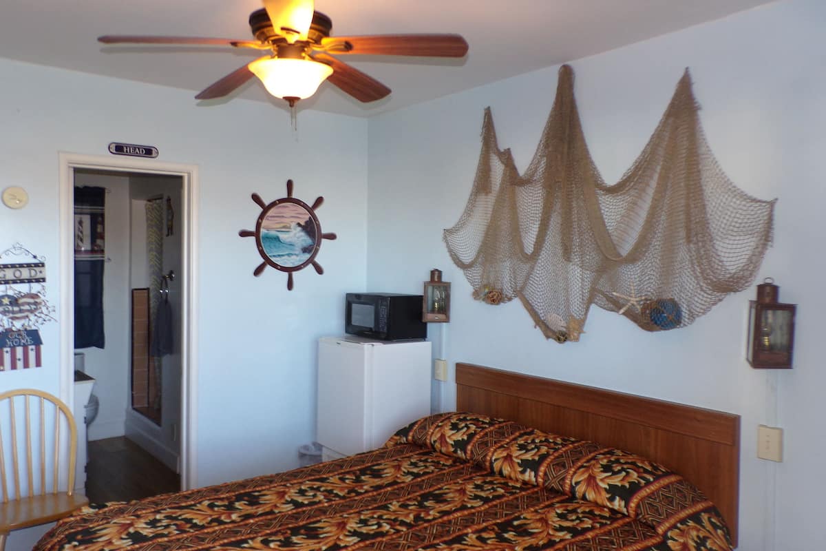 A bedroom with a bed, a ceiling fan, a wall-mounted TV, and a door leading to a bathroom.