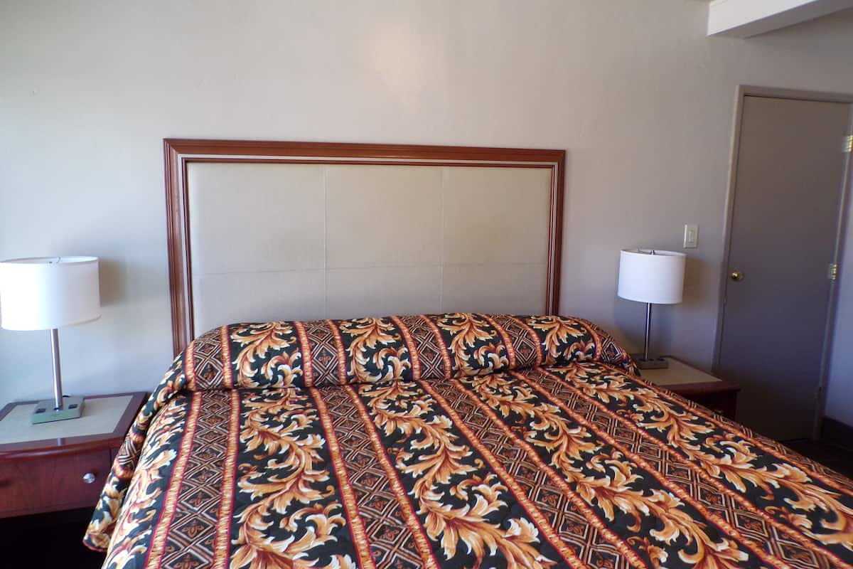 A hotel room with a large bed, two bedside lamps, a wooden headboard, and a door.
