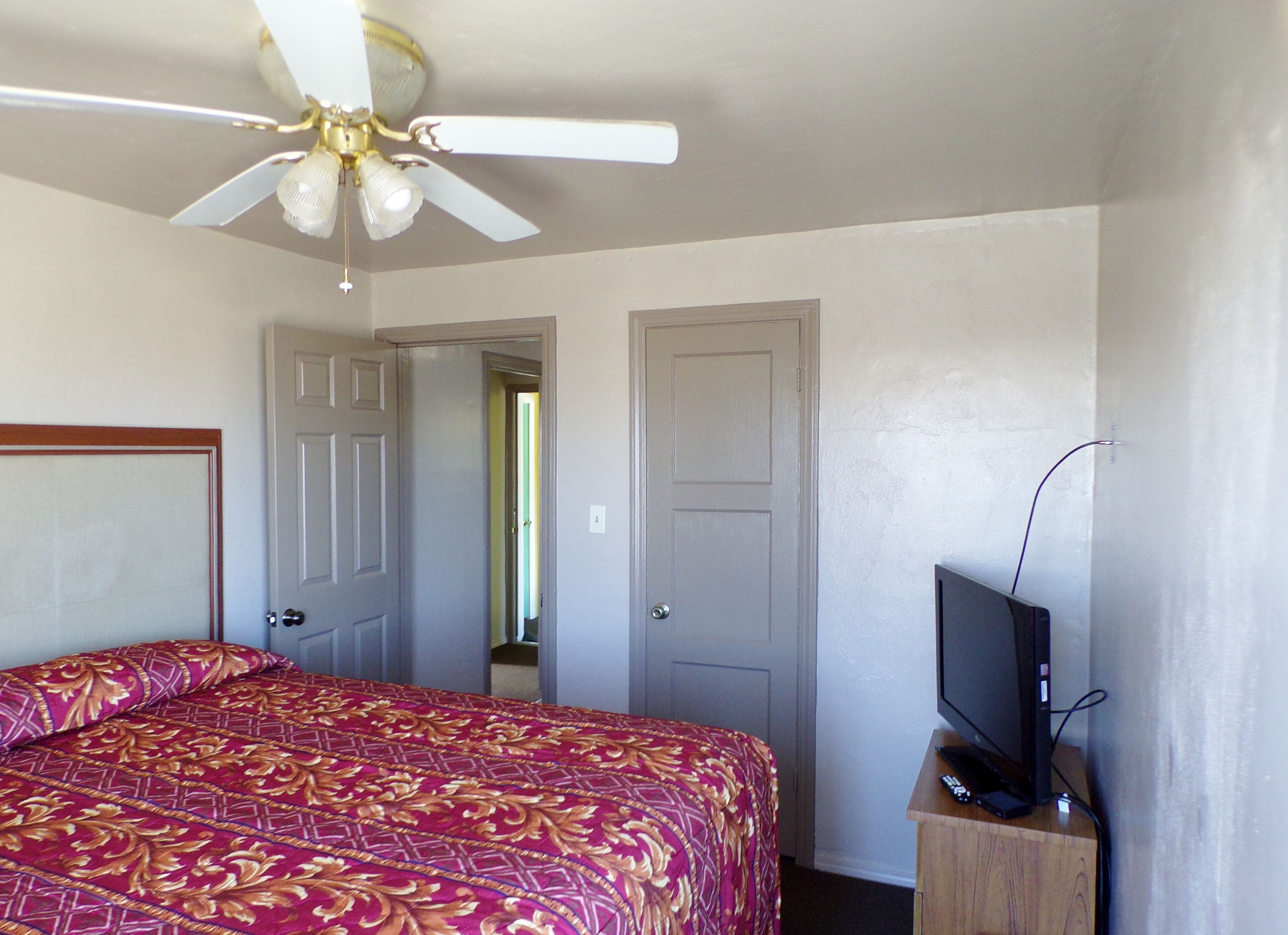 A bedroom with a bed, a ceiling fan, a television on a wooden stand, and two doors.