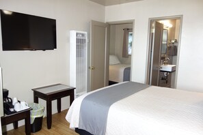 Ein Hotelzimmer mit Bett, Fernseher, Schreibtisch mit Kaffeemaschine, Mülleimer und einem durch eine offene Tür einsehbaren Badezimmer.