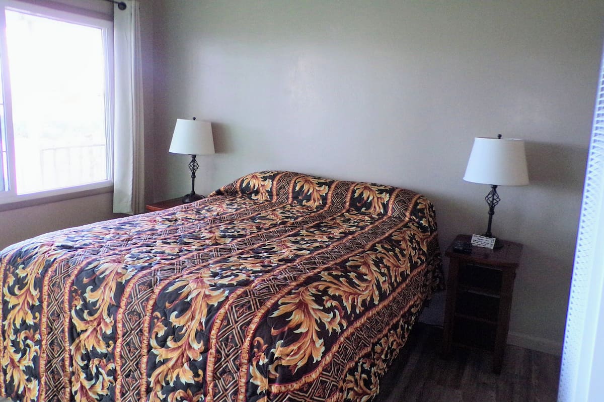 A neatly made bed with a patterned bedspread, two bedside lamps, and a window with curtains.