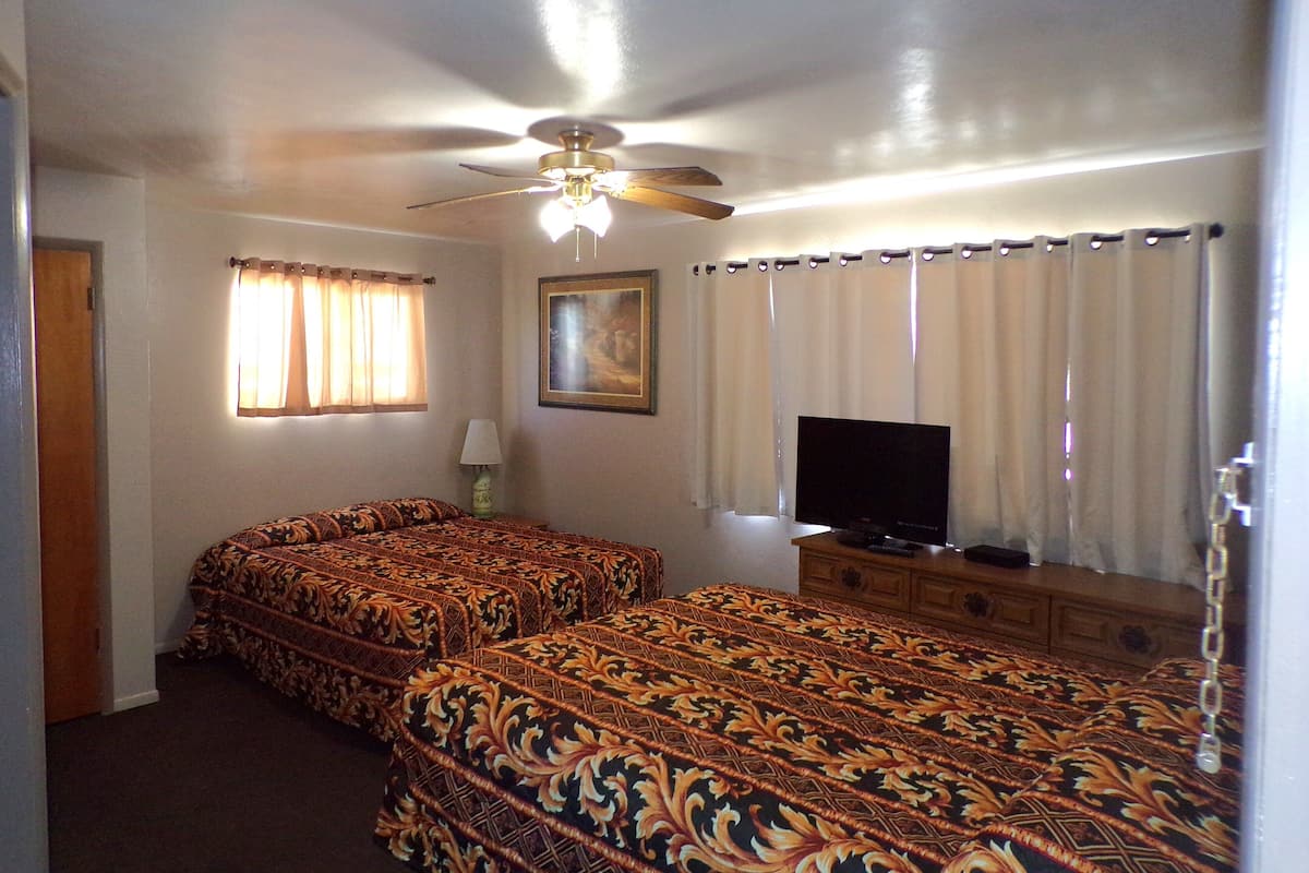 A hotel room with two beds, a ceiling fan, a television, and a painting on the wall.