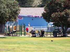 Un parque infantil con diversas estructuras de juego, incluyendo toboganes y juegos de escalada, rodeado de césped.