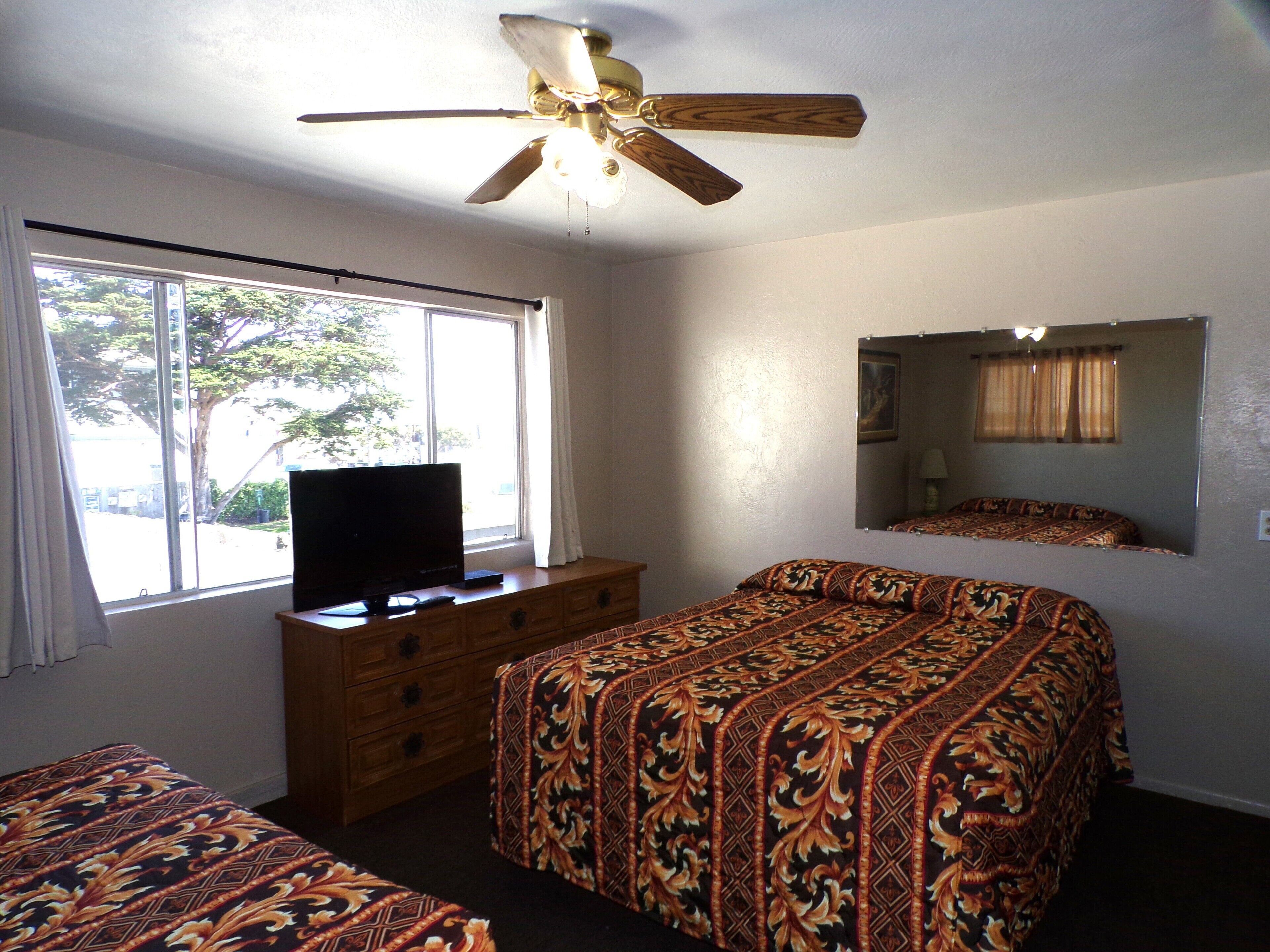 A bedroom with a bed, a dresser, a television, a ceiling fan, a window, and a mirror.