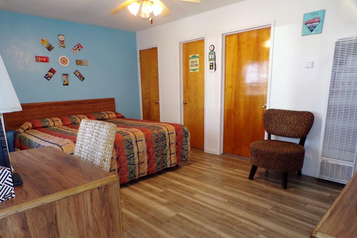 A room with a bed, a chair, a desk, and a wall with cards. There are two doors, one labeled 'REST ROOM' and another with a sign.