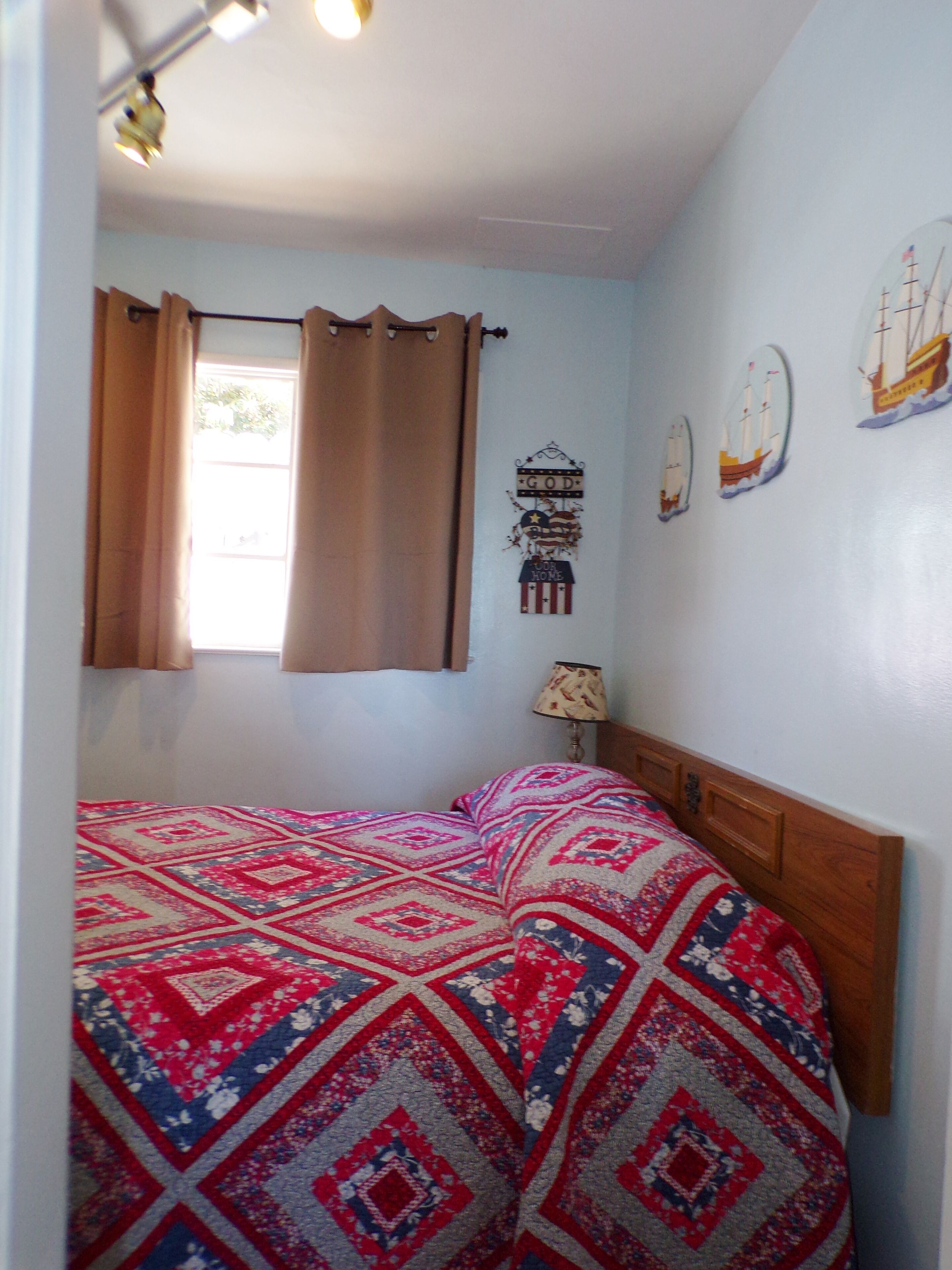 Un dormitorio con cama, cortinas, una lámpara y adornos en la pared.