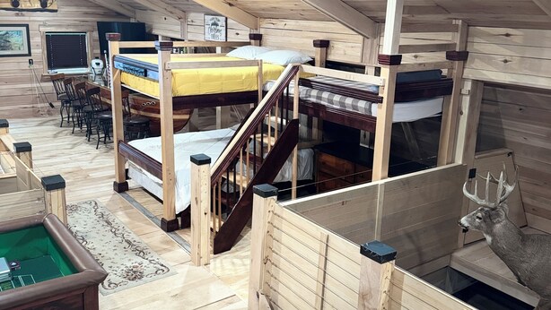 Uma cabana de madeira com beliches, mesa de bilhar e um troféu de cabeça de veado.