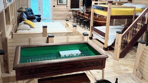 Interior acolhedor de uma cabana com mesa de bilhar, móveis de madeira e escada para um mezanino.
