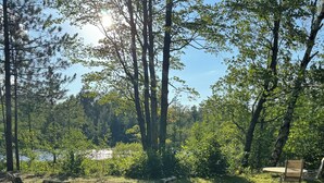 Uma área de piquenique com mesa e cadeiras numa área arborizada, com um lago ao fundo.