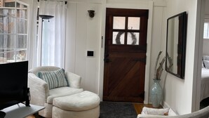 A living room with a wooden floor, a white sofa, a grey sofa, a TV, and a wooden door. - Cozy get-away in Pacific Grove (Pet Friendly!) (Pacific Grove)