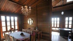 Interior em madeira com uma mesa de jantar, cadeiras, um candelabro e janelas amplas.
