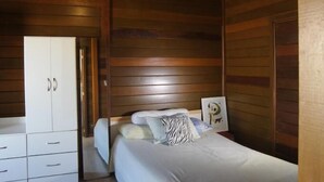 Quarto de cabana de madeira com cama, guarda-roupa e luminária pendente.