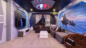 A modern living room with a starry ceiling, a large flat-screen TV, a sofa, and a plush toy. - 8 Bdrm Villa w/Pool, Theater Near Disney w/ Waterpark & Free Shuttle Service (Kissimmee)