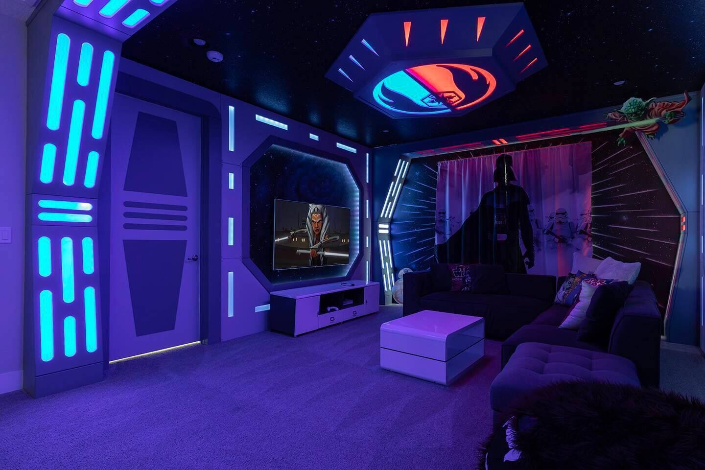 A room with a large screen, a sofa, and a unique ceiling design.