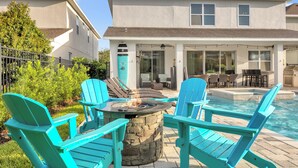A patio with a stone fire pit, turquoise Adirondack chairs, and a pool area. - 8 Bdrm Villa w/Pool, Theater Near Disney w/ Waterpark & Free Shuttle Service (Kissimmee)