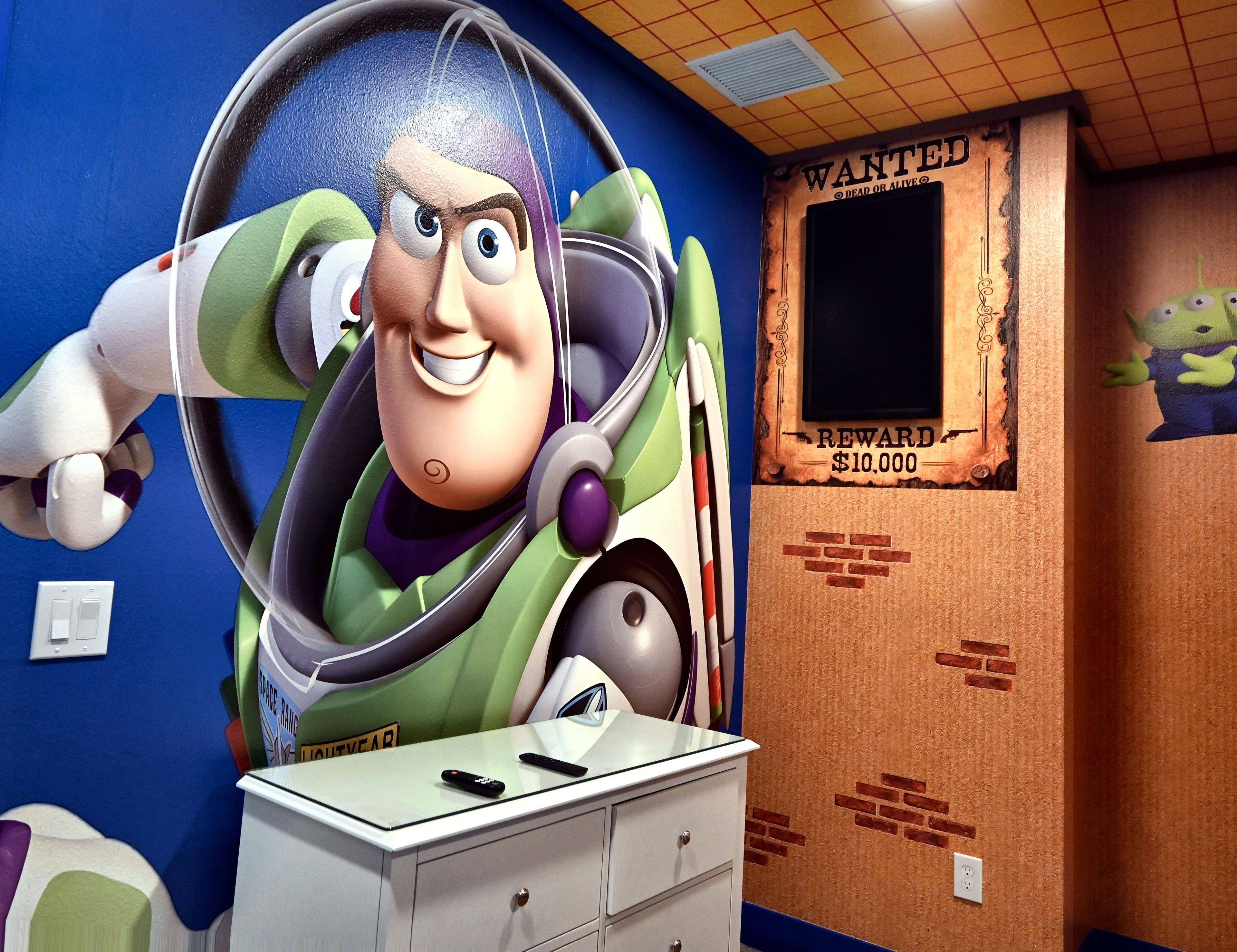 A room with a large space-themed mural, a dresser with a remote control, and a 'WANTED' poster on the wall.