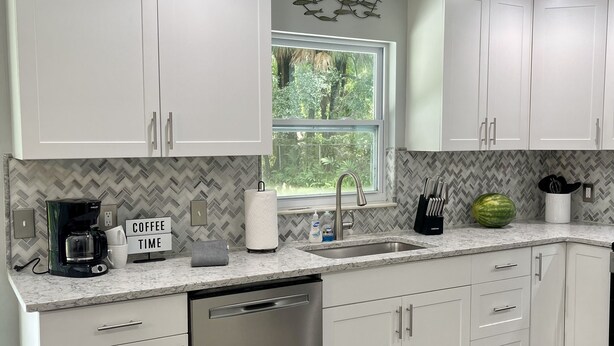 A modern kitchen with white cabinets, a stainless steel dishwasher, and a herringbone-patterned backsplash. - Crystal River Getaway , Free Kayaks + Minutes to Three Sisters Springs. Pet ok  (Crystal River)