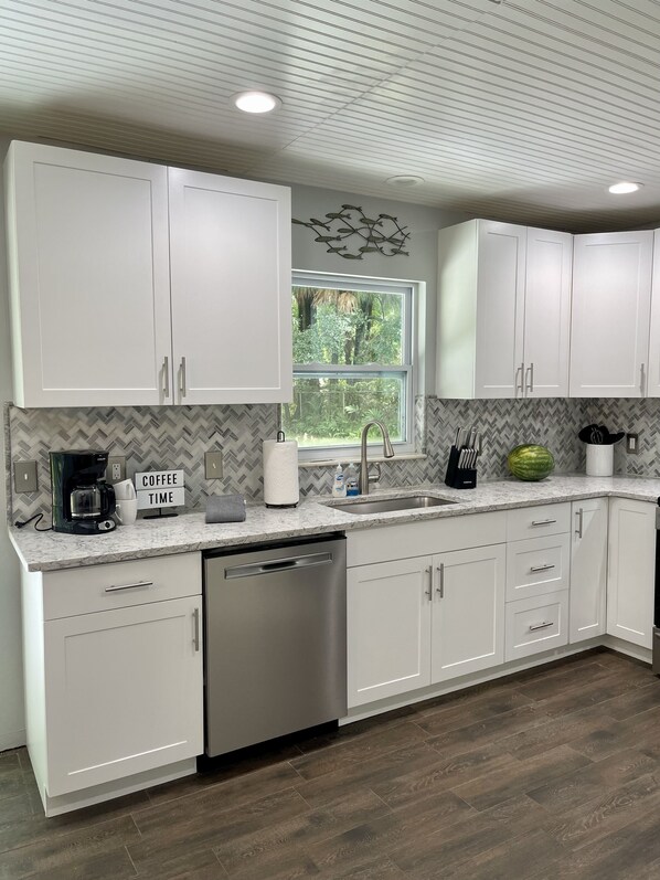 A modern kitchen with white cabinets, a stainless steel dishwasher, and a herringbone-patterned backsplash.