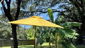 A patio area with wicker furniture, a glass table, and a yellow umbrella. - Crystal River Getaway , Free Kayaks + Minutes to Three Sisters Springs. Pet ok  (Crystal River)