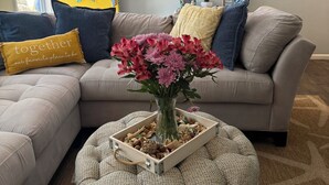 Un salon avec un canapé, une table basse ornée d’un vase de fleurs, une porte jaune décorée d’une image de sirène et un tableau représentant l’océan.