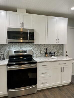 A modern kitchen with white cabinetry, a stainless steel refrigerator, a microwave, and an oven.