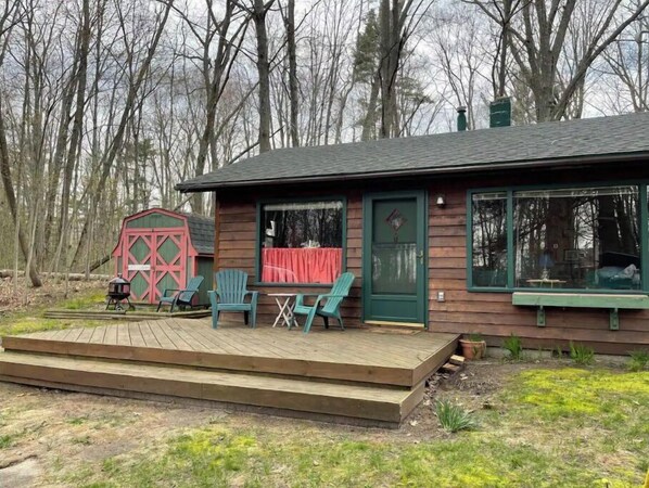 Eine Holzhütte mit Veranda, zwei Stühlen und einem rotfarbenen, auf einen Bauernhof abgestimmten Gebäude im Hintergrund.