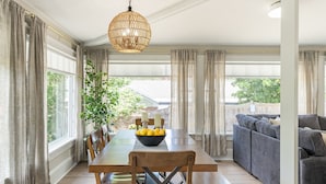 A spacious dining area with a wooden table and chairs, a bowl of lemons, and a large window with curtains.