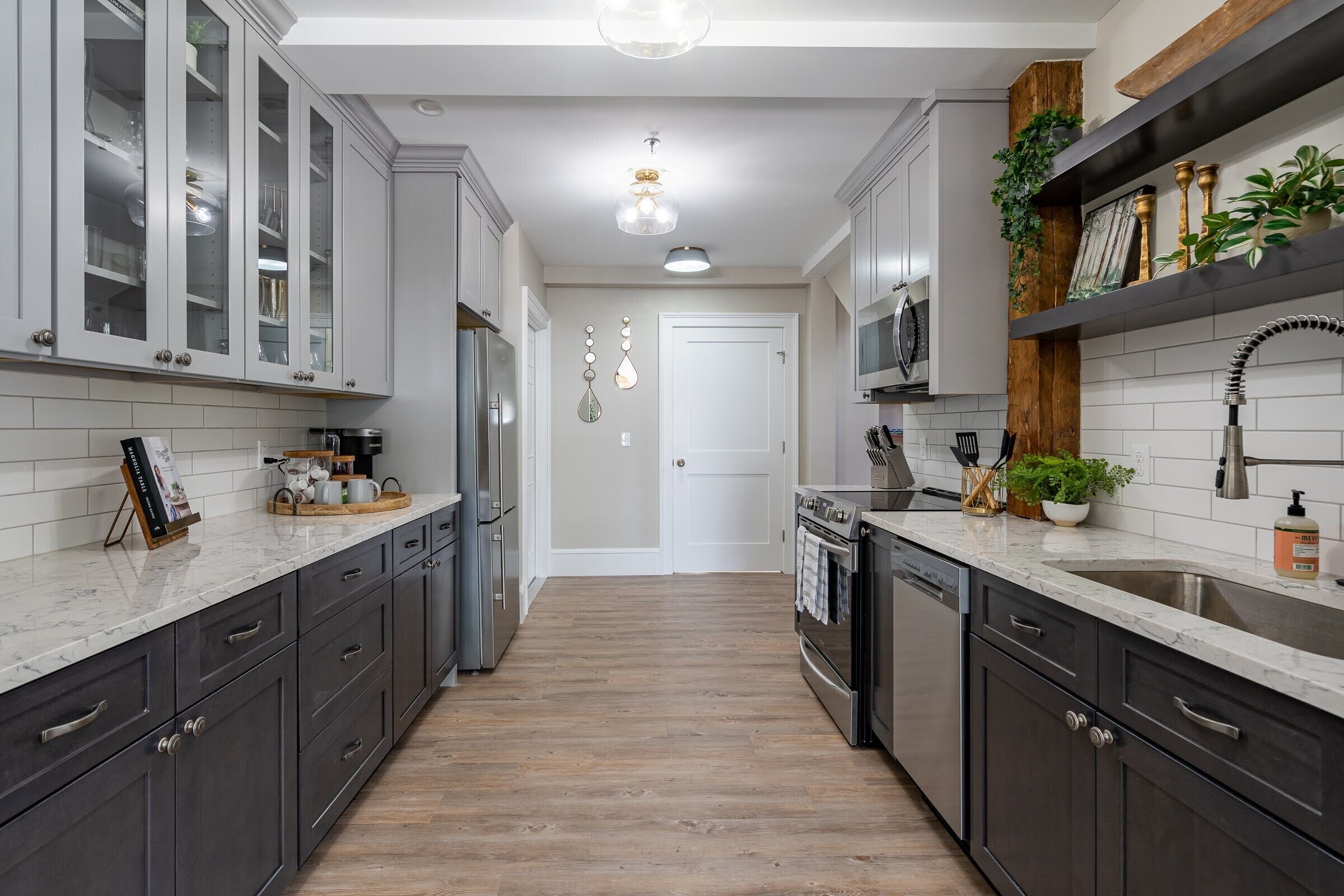 A modern kitchen with dark cabinets, white countertops, and a wooden floor.