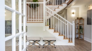 A staircase with white railings and wooden steps, leading to an upper floor. There are two cushioned benches at the bottom of the stairs.