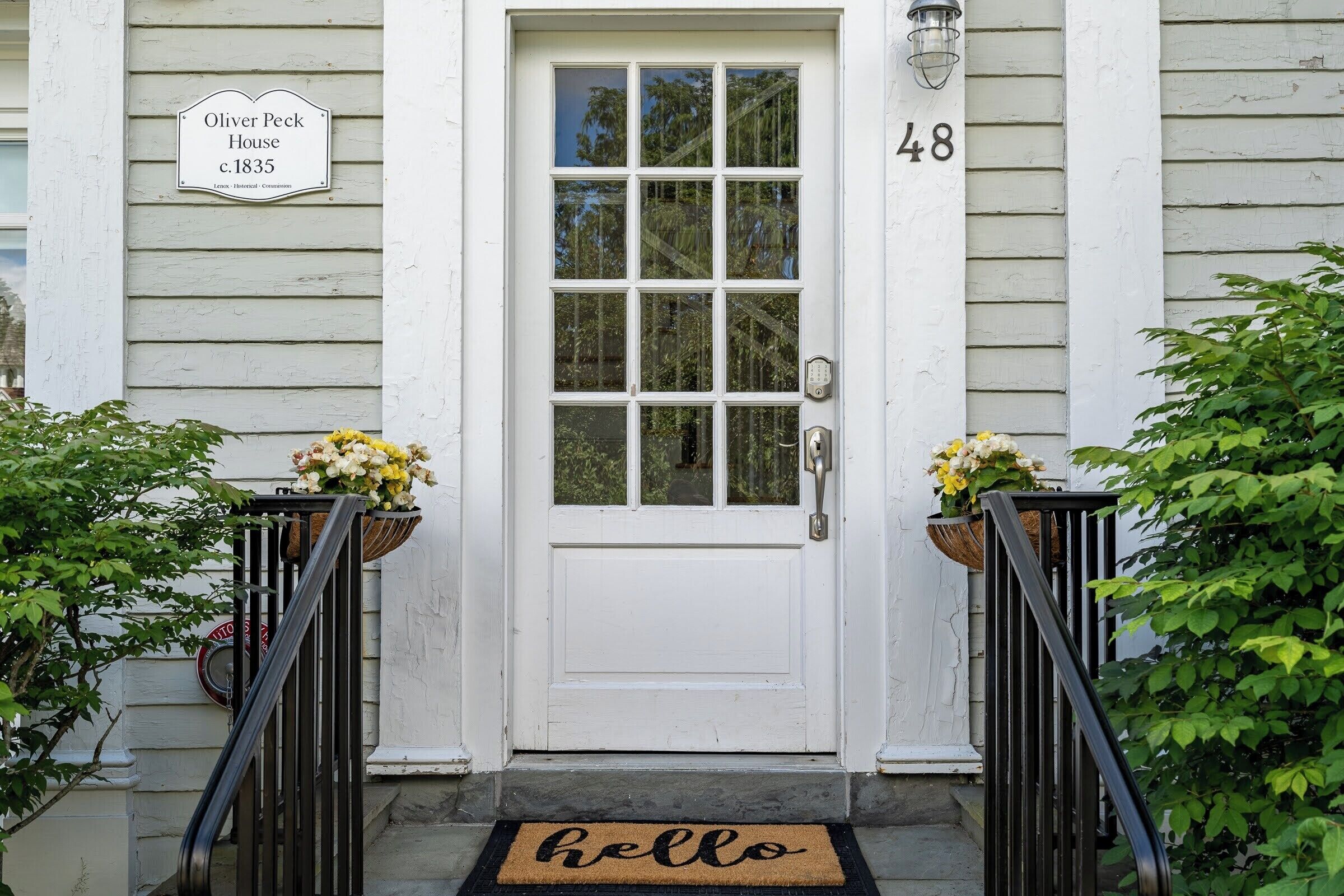 Une maison blanche avec une porte d’entrée, le numéro 48, et un paillasson sur lequel est écrit « Bonjour ».