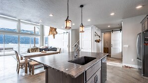 A modern kitchen with a large island, pendant lighting, and a view of the outdoors. - New Lakefront Modern Chalet With Panoramic Views (Donnelly)