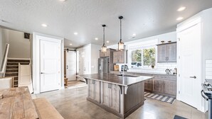 A spacious kitchen with a large island, wooden cabinets, and pendant lighting. - New Lakefront Modern Chalet With Panoramic Views (Donnelly)