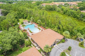An aerial view of a resort with a swimming pool surrounded by palm trees and a parking area.
