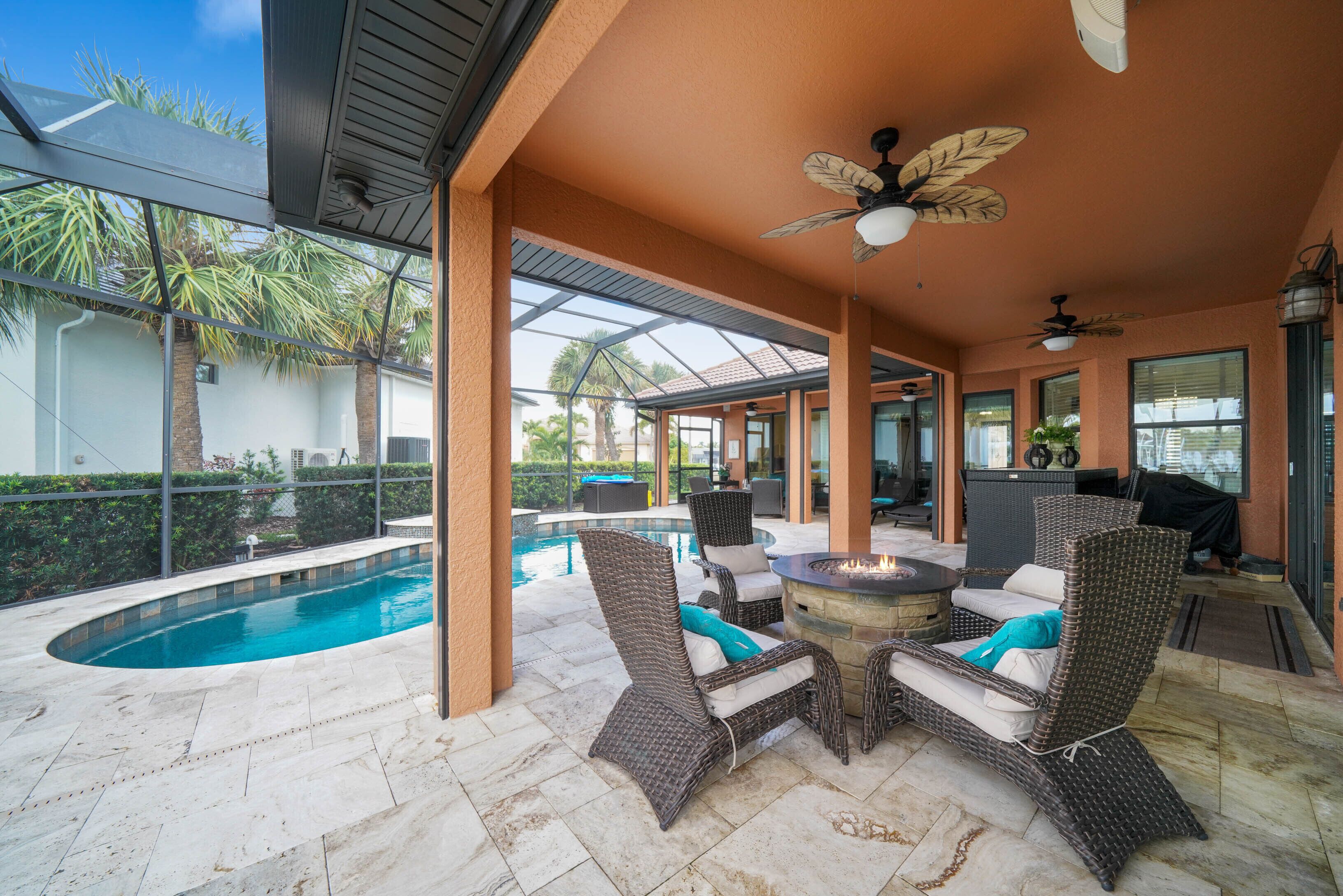 Une terrasse extérieure avec une piscine, des meubles en osier et des ventilateurs de plafond.