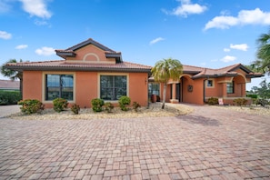 A two-story house with a red-tiled roof, large windows, and a paved driveway.