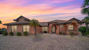 A two-story house with a brick driveway, a front entrance, and a landscaped garden. - Beautiful Gulf Access home Amazing pool sunsets  (Punta Gorda)