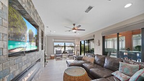 A modern living room with a stone fireplace, leather sofa, and a large flat-screen TV. - Beautiful Gulf Access home Amazing pool sunsets  (Punta Gorda)