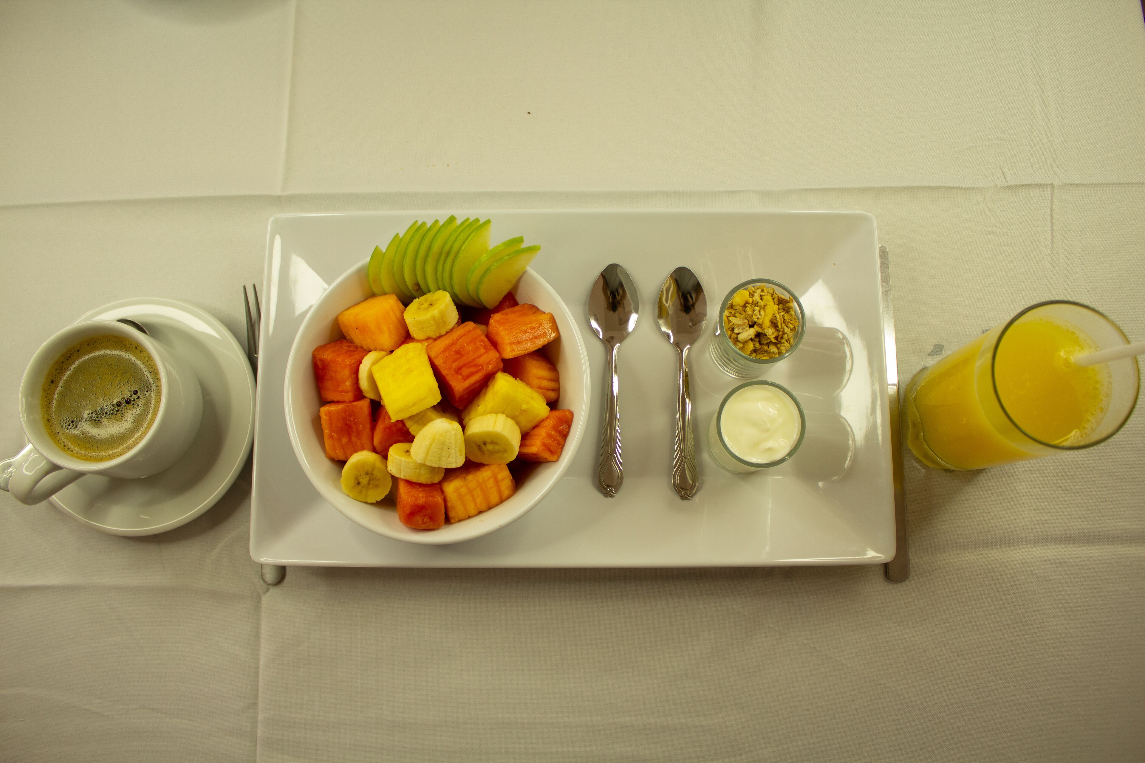 Bandeja de desayuno con un tazón de fruta, una taza de café, un vaso de jugo de naranja y salsas.