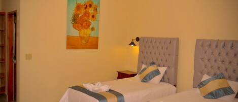 A hotel room with two beds, a painting of sunflowers, an air conditioner, and a bedside lamp.