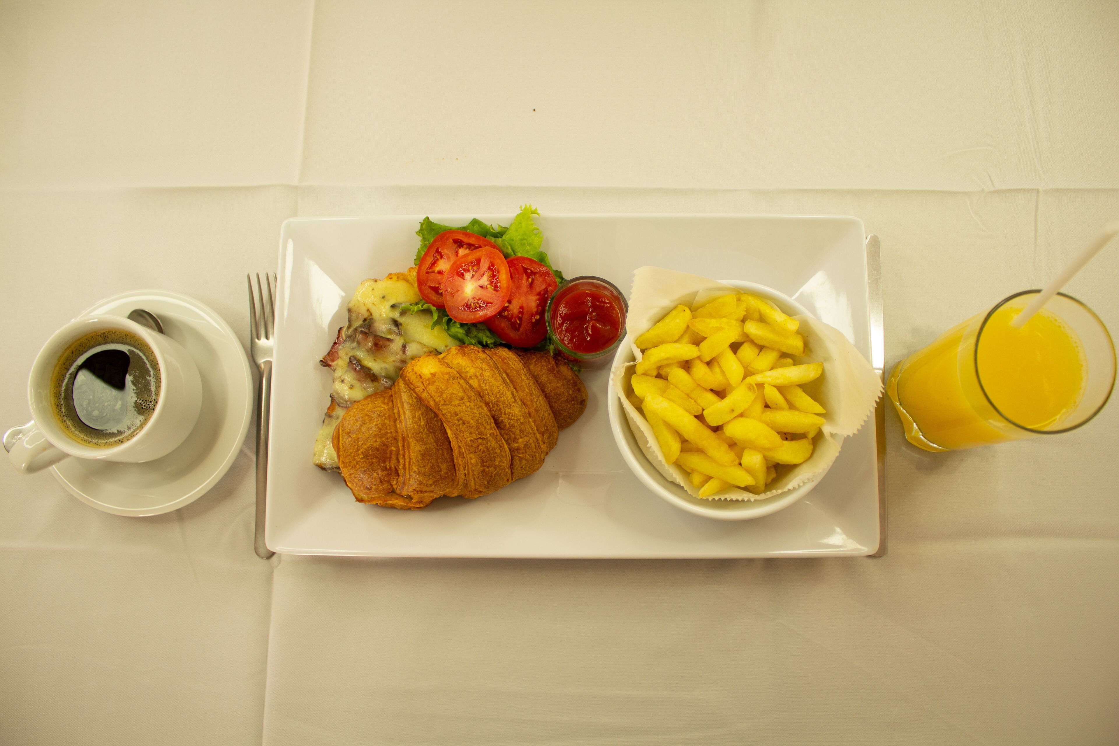 Een bord met een croissant, salade en frietjes, een kop koffie en een glas sinaasappelsap.