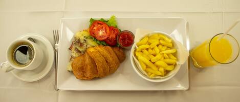 A plate with a croissant, salad, and French fries, a cup of coffee, and a glass of orange juice.