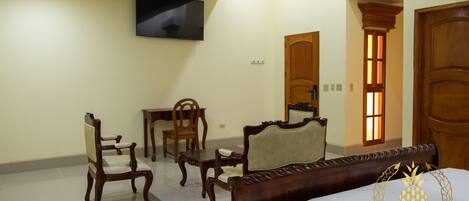 Quarto de hotel com cama, duas cadeiras, uma mesa e televisão na parede.