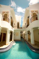 Interior de hotel con piscina central, varios balcones y un emblema decorativo en la pared.