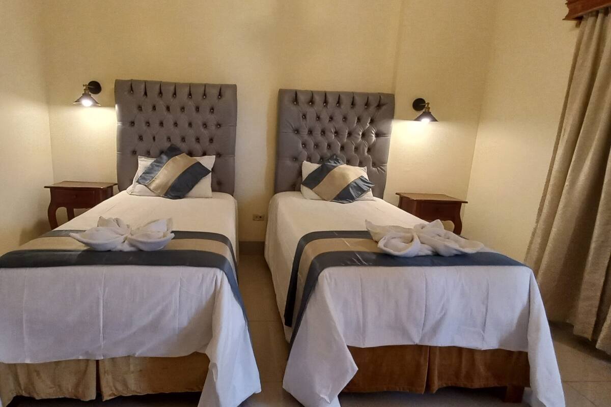 Ein Hotelzimmer mit zwei Betten, jeweils mit einem gesteppten Kopfteil, Nachttischlampen und Handtüchern.