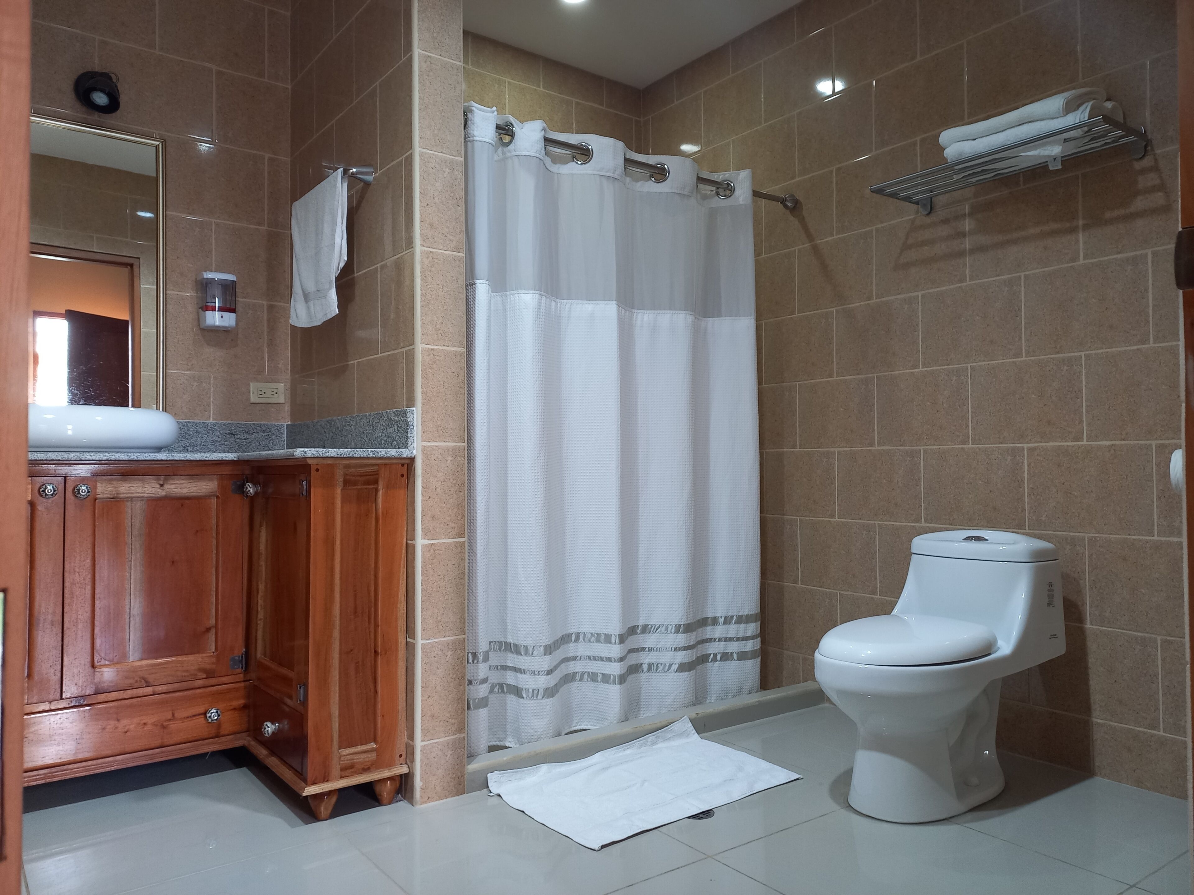 A bathroom with a wooden vanity, a white toilet, a shower curtain, and a towel rack.