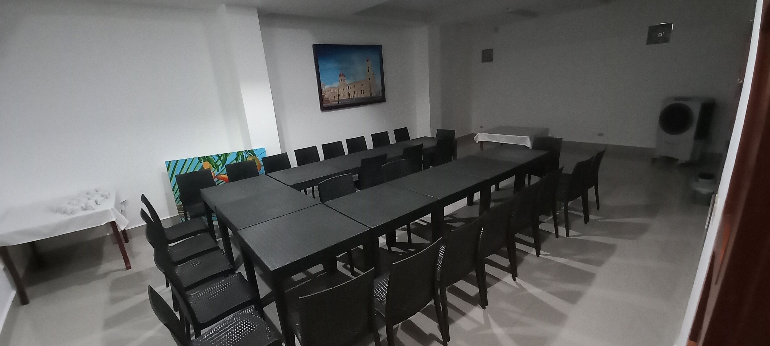 A conference room with a long table and chairs, a painting on the wall, and an air conditioning unit in the corner.