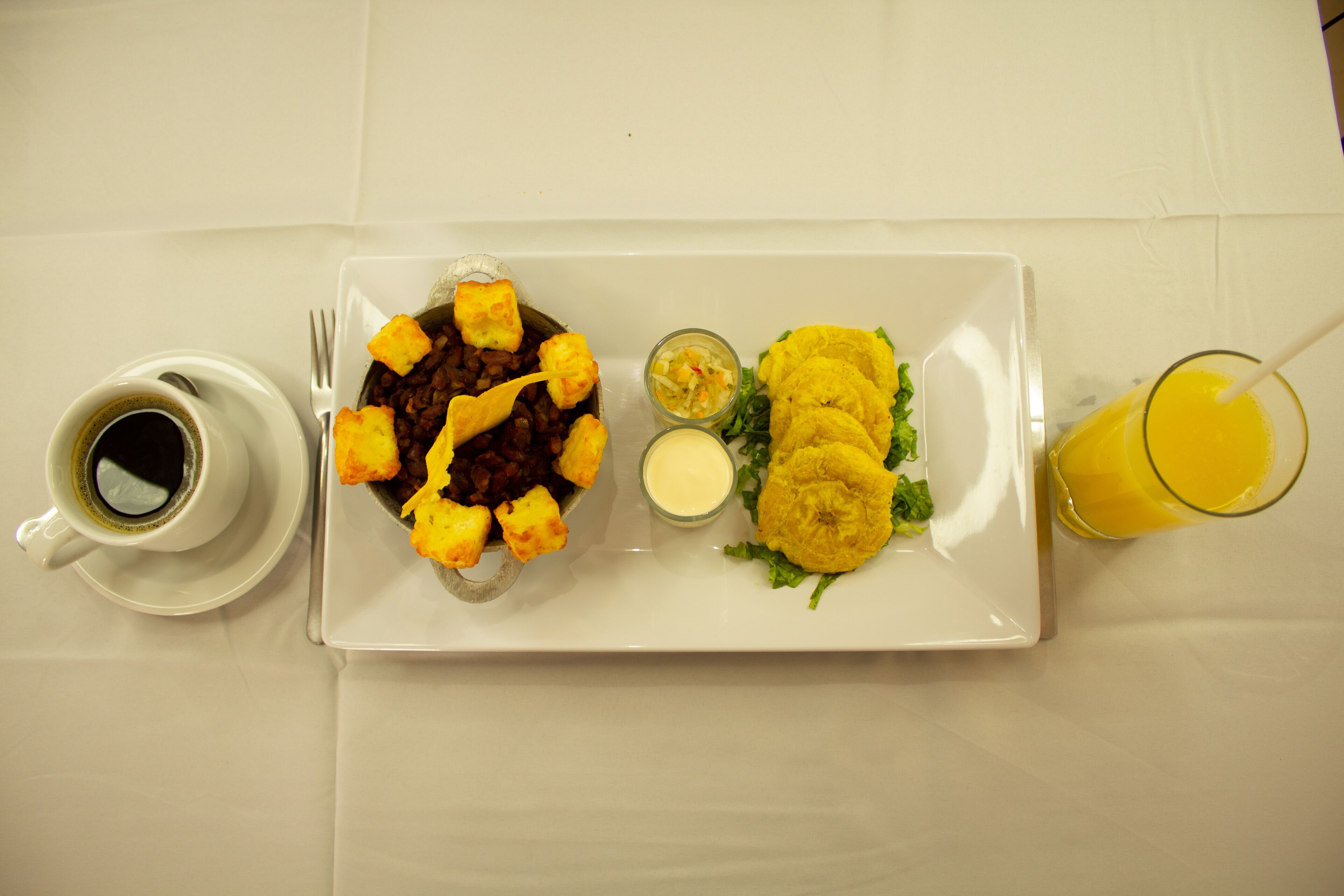 A white table with a plate of food, a cup of coffee, and a glass of orange juice.