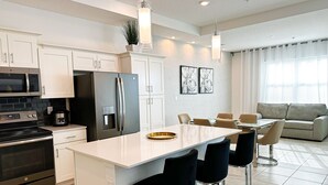 Une cuisine moderne avec des meubles blancs, un îlot central doté de tabourets, un réfrigérateur et un four à micro-ondes.